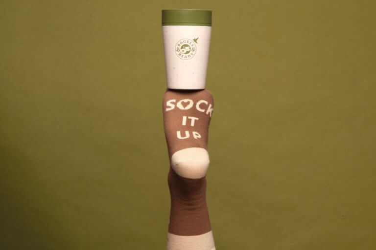 Voet in een Bagels & Beans sok balanceert een koffie.